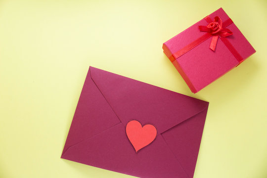 Dark red triangle envelope with large red heart on yellow background with gift box Valentine's day or festive concept Letter or invitation inside closed envelope Minimalist concept with free space