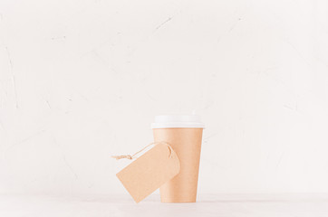 Obraz premium Coffee packing mockup - craft brown paper cup with white cap and blank label on white wood board, coffee shop interior. Modern elegant concept for branding identity, advertising, design.