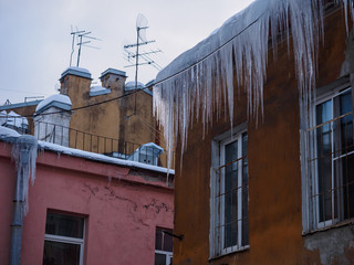 large long ice icicles hang on the edge of the roof on old houses