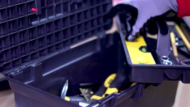 A close up of a toolbox full with tools. A hand of a handyman opens it and picks out a few tools out of it.
