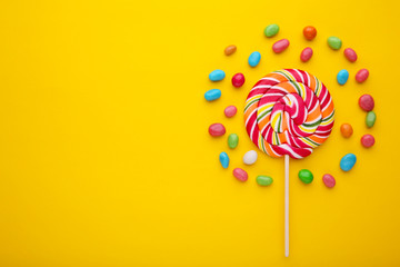 Colorful lollipops and different colored round candy on yellow background