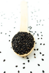 Black sesame on wooden spoon isolated on white background.