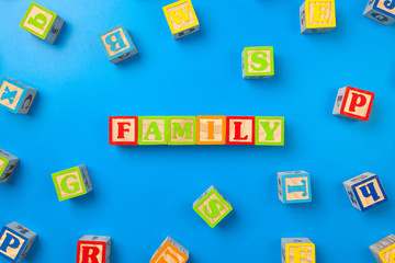 Family. Wooden colorful alphabet blocks on blue background, flat lay, top view.