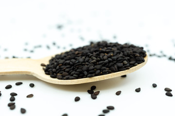 Black sesame on wooden spoon isolated on white background.