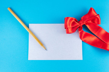 A blank silver letter with a wooden pencil and big red bow on a blue background Letter or invitation Minimalist concept Copy Space and template