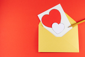Yellow open envelope with white blank letter inside Big and small hearts red white color with wooden pencil on a red background Letter or invitation Minimalist concept Copy Space and template