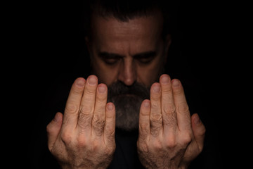 Man raising hands in prayer, in a dark room and with black background