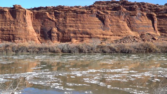 View of ice floating down the Colorado River in Moab Utah with red rock cliffs reflecting in the water.