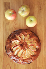 Homemade apple cake and fresh apples top view on wooden table.