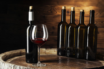 Bottle and glass of red wine on wooden barrel shot with dark wooden background