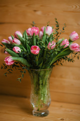A bouquet of pink tulips in a beautiful crystal vase on wooden background. Spring