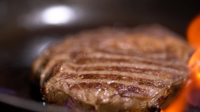 Delicious juicy steak fried in a griddle on fire close up. Camera moves from left to right.