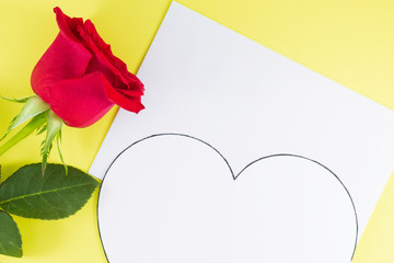 A fresh red rose big bud and petals with green leaves near white empty letter and big white heart Yellow background Invitation or Felicitation Minimalist concept Copy Space and template