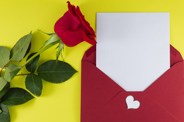 A fresh red rose big bud and petals with green leaves near white empty letter in dark red open envelope Yellow background Invitation or Felicitation Minimalist concept Copy Space and template