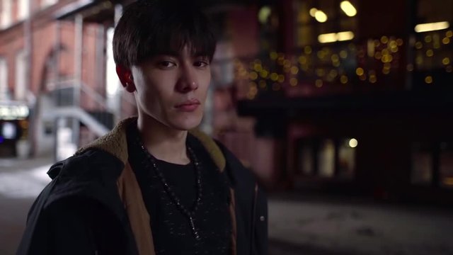 portrait of a thin Asian guy with pronounced cheekbones on the background of the city and lights