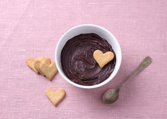 Bowl of delicious chocolate mousse and heart cookies for Valentine's Day on a pink textile background