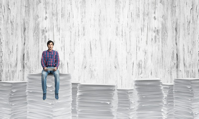 Attractive man sitting on pile of paper documents.