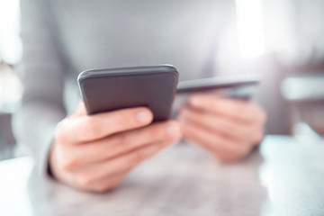 Young woman shopping online with credit card using smartphone at home. Indoor.