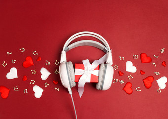 White headphones with gift box and decorative hearts on a red background. St. Valentines Day music gift concept.