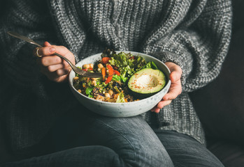Healthy vegetarian dinner. Woman in grey jeans and sweater eating fresh salad, avocado half,...
