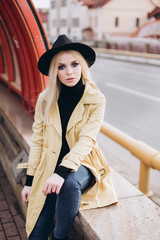 Street fashionable close up portrait of young hipster girl in yellow suit and black hat outdoors