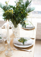Beautiful springtime table setting with green leaves and mimosa branches, bright white table dinner decoration
