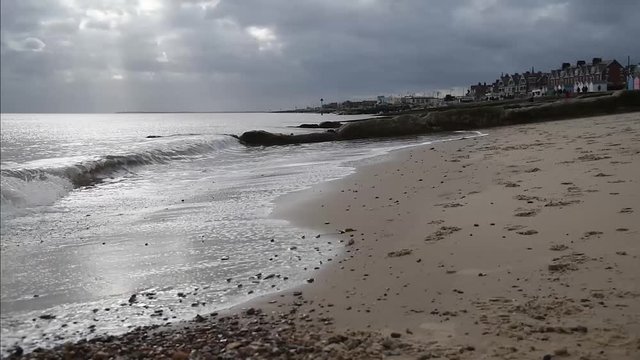 Waves breaking on Felixstowe beach with sun rays appearing through cloud