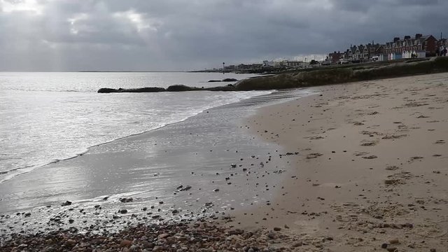 Waves breaking on Felixstowe beach with sun rays appearing through cloud