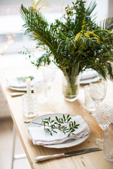 Beautiful springtime table setting with green leaves and mimosa branches, bright white table dinner decoration