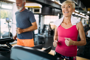 Senior people running on a treadmill in health club.