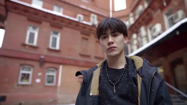 portrait of an Asian guy in the winter on the street against the houses.