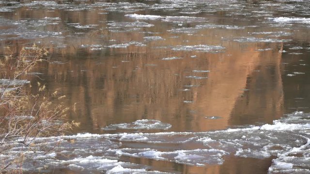 Cliff reflecting in Colorado River as ice floats downstream through Moab Utah.