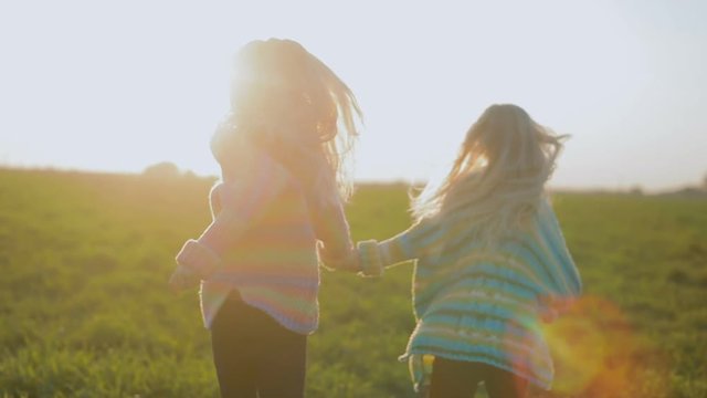 slow motion backside view joyful blond little twin sisters join hands and run in wide meadow at sunlight