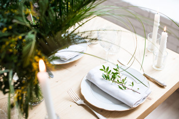 Beautiful springtime table setting with green leaves and mimosa branches, bright white table dinner decoration