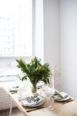 Beautiful springtime table setting with green leaves and mimosa branches, bright white table dinner decoration