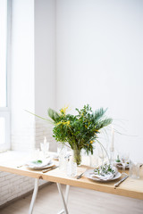 Beautiful springtime table setting with green leaves and mimosa branches, bright white table dinner decoration