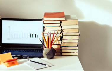 Laptop, stack of books, notebooks and pencils on white table, education office concept background.