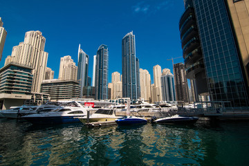 Obraz na płótnie Canvas Dubai, United Arab Emirates - October, 2018: Modern skyscrapers and water channel with boats of Dubai Marina at sunset, United Arab Emirates