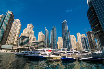 Fototapeta premium Dubai, United Arab Emirates - October, 2018: Modern skyscrapers and water channel with boats of Dubai Marina at sunset, United Arab Emirates