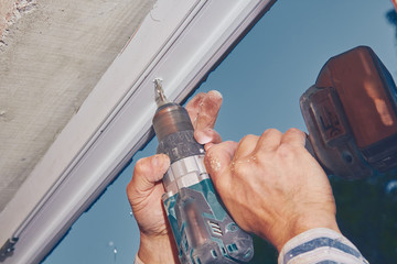 Worker using battery hand drill to screw into the PVC window frame.