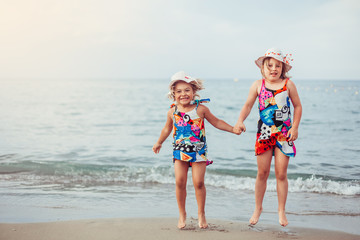 Two adorable sisters playing and having fun on the beach. Childhood, vacation, joy, happiness, frienship concept