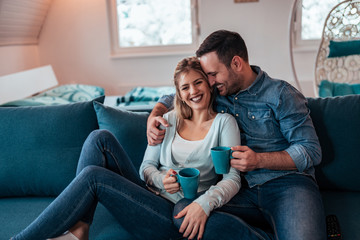 Beautiful couple in casual wear drinking tea on sofa at modern, cozy apartment.