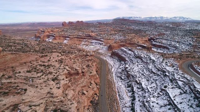 Aerial view above car driving on road through desert terrain in Moab Utah with the road splitting the snow on the landscape.