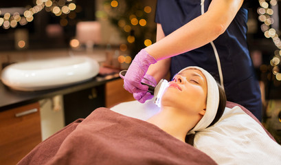Obraz na płótnie Canvas people, beauty, cosmetic treatment, cosmetology and technology concept - beautician with microdermabrasion device doing face exfoliation to young woman lying at spa parlor