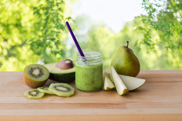 baby food, healthy eating and nutrition concept - glass jar with green fruit puree on wooden board over natural background