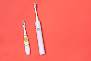 Adult and baby electric toothbrushes on pink coral background. Dental care