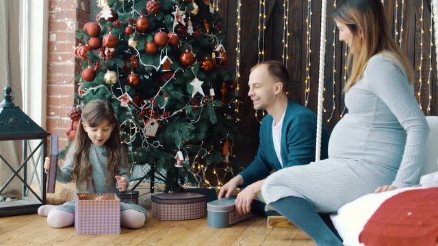 The little girl, dad and pregnant mom near the Christmas tree