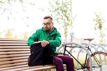 travel, tourism and people concept - man or hipster with backpack sitting on city street bench