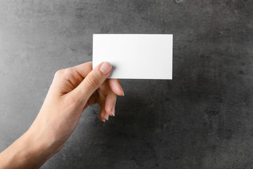 Female hand with blank business card on grey background