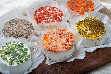 Assortment of French fresh white soft goat cheeses with different tastes topping made with herbs, paprika, indian curry, bruscetta, chives and dried tomatoes